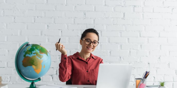 Person bei einem Schreibtisch mit Laptop und Arbeitsmaterial